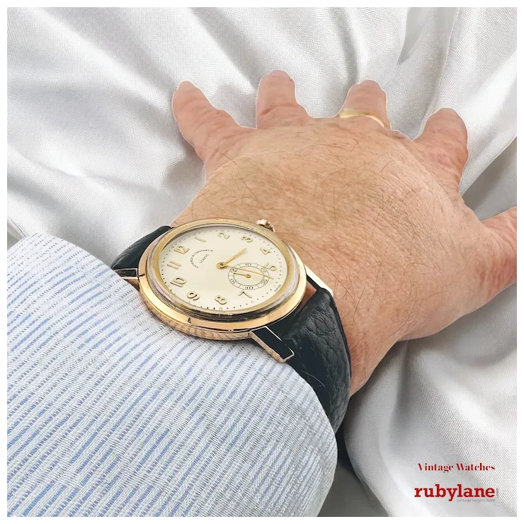 Hand wearing a vintage watch with a white background, featuring Rubylane branding.