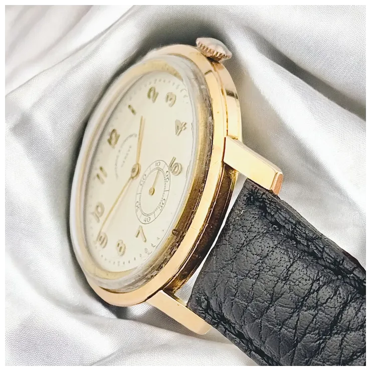 Gold watch with a black leather strap on a white fabric background