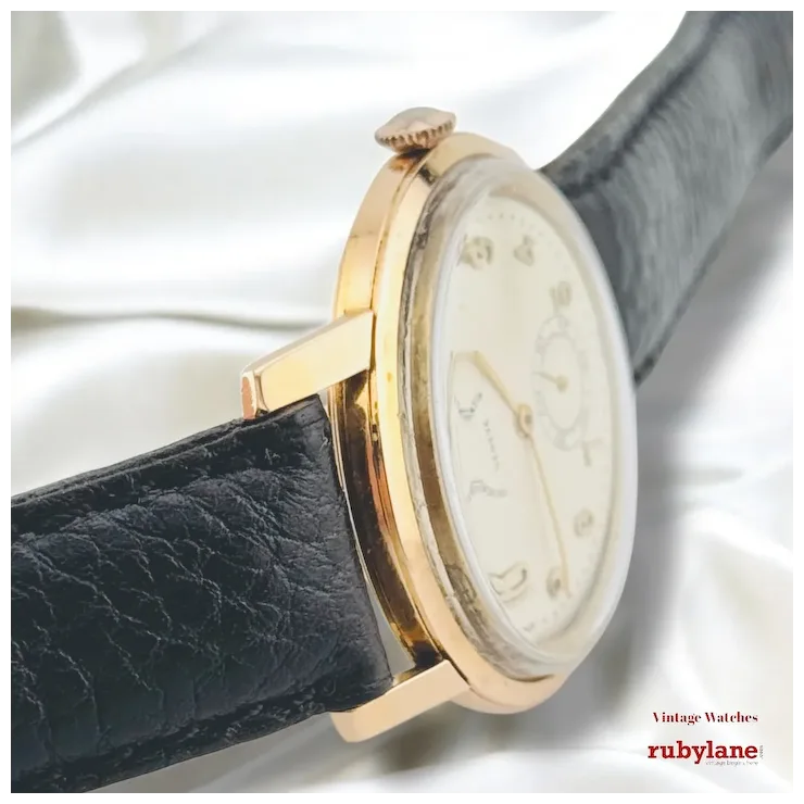 Vintage watch with gold case and black leather strap on a white background, featuring Ruby Lane branding.