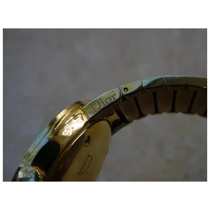 Close-up of a gold watch band with 'Dior' branding on a blurred background