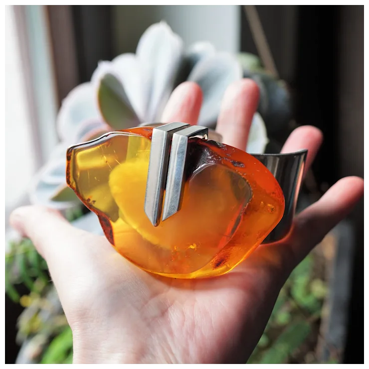 Hand holding a unique orange and silver object with a blurred plant background