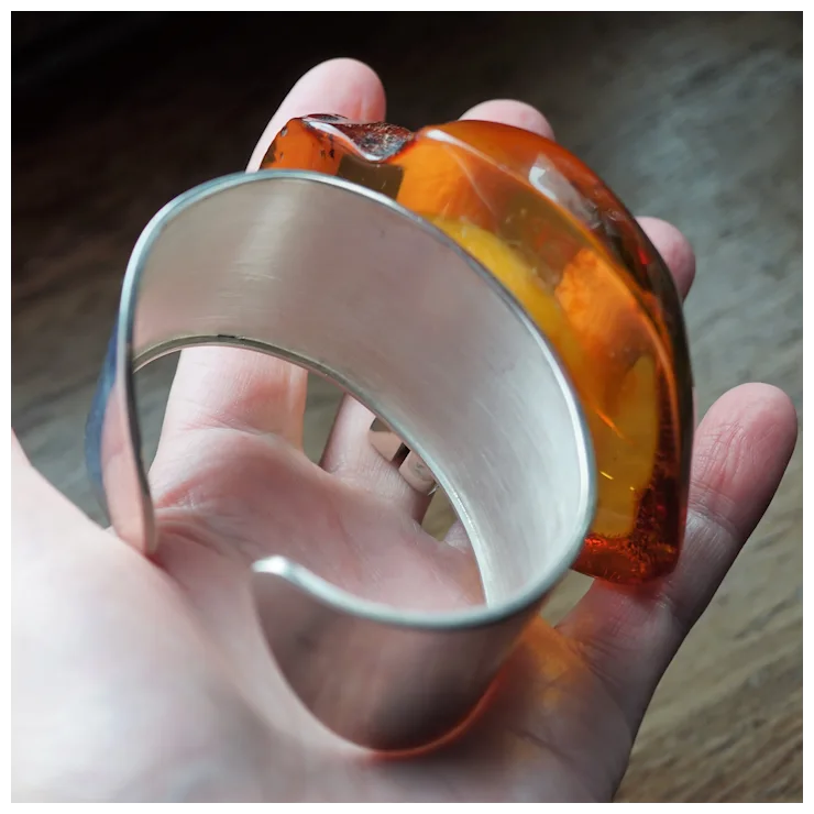 Hand holding a bracelet with orange and silver design