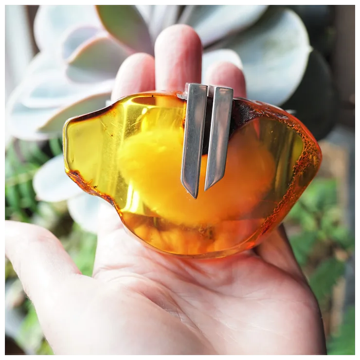 Hand holding a yellow and silver object with a blurred plant background