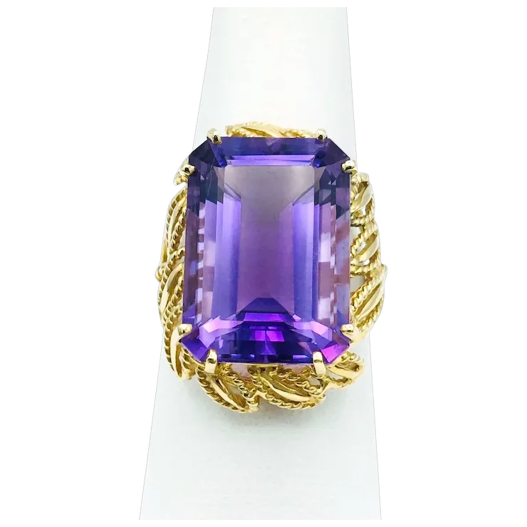 Gold ring with a large purple gemstone on a white stand