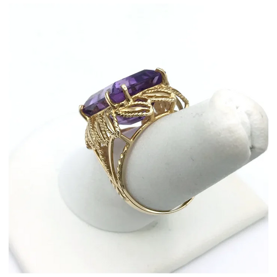 Gold ring with a purple gemstone on a white stand