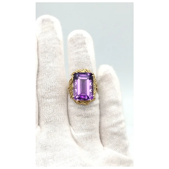 Ring with a purple gemstone held by a gloved hand on a light gray background