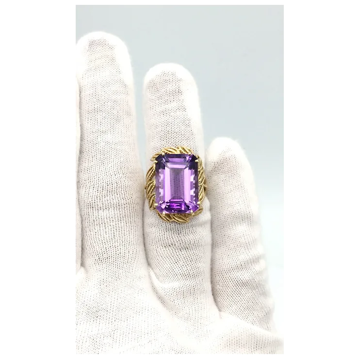 Ring with a purple gemstone held by a gloved hand on a light gray background