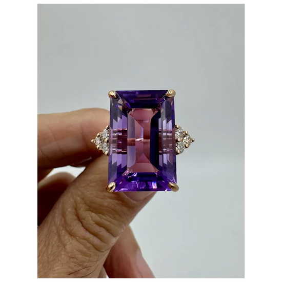 Amethyst ring with gold setting held by a hand against a gray background