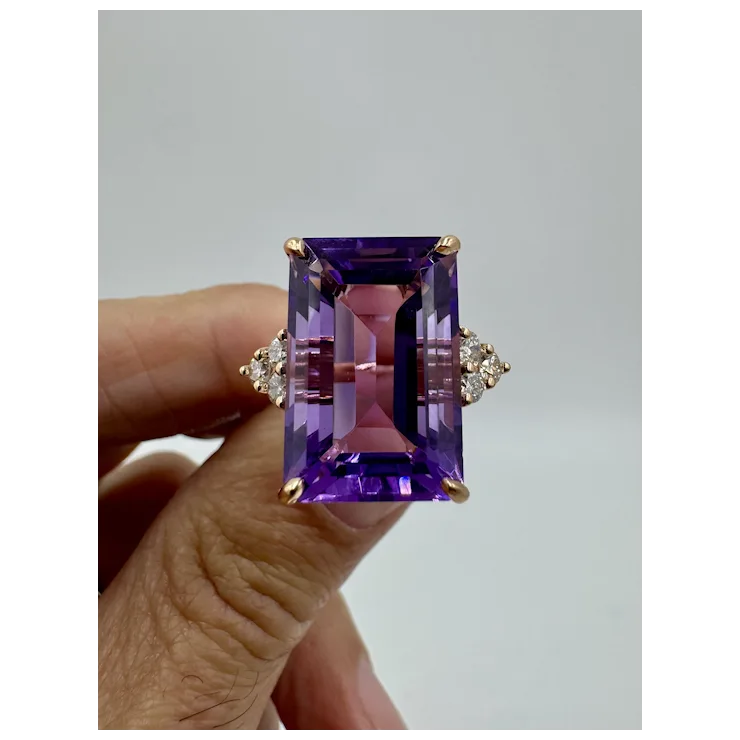 Amethyst ring with gold setting held by a hand against a gray background