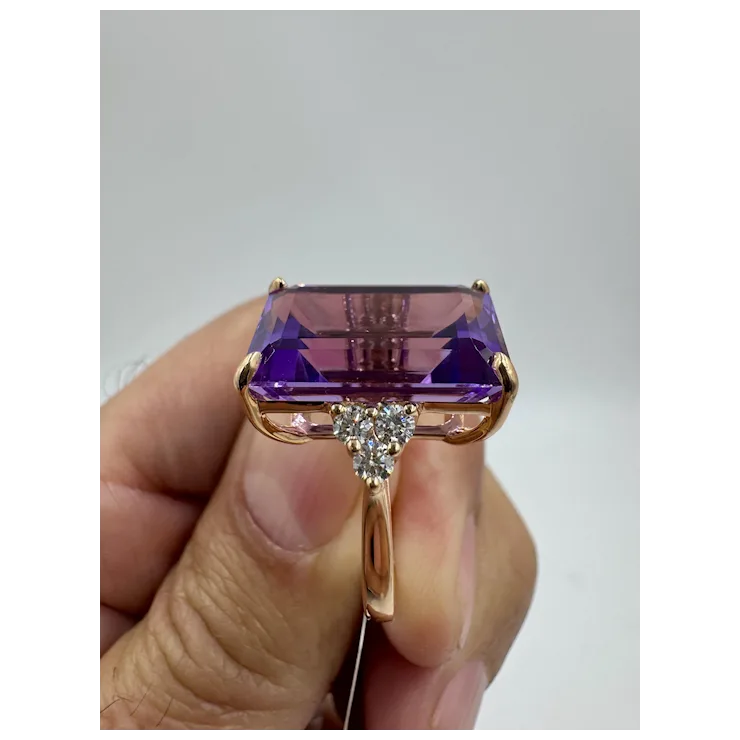 Gold ring with a large purple gemstone held by a hand against a gray background