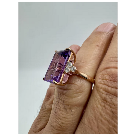 Ring with a purple gemstone and small diamonds on a finger against a light gray background