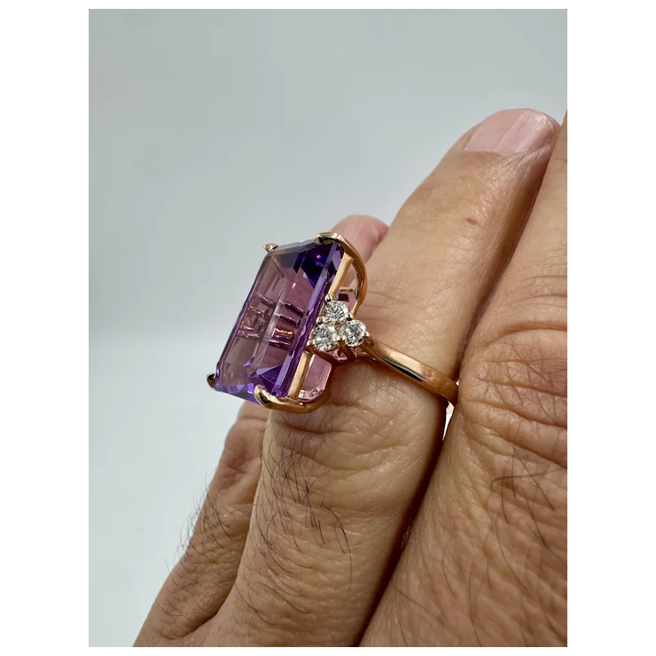 Ring with a purple gemstone and small diamonds on a finger against a light gray background