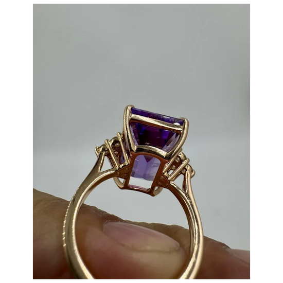 Gold ring with purple gemstones held by a hand against a gray background