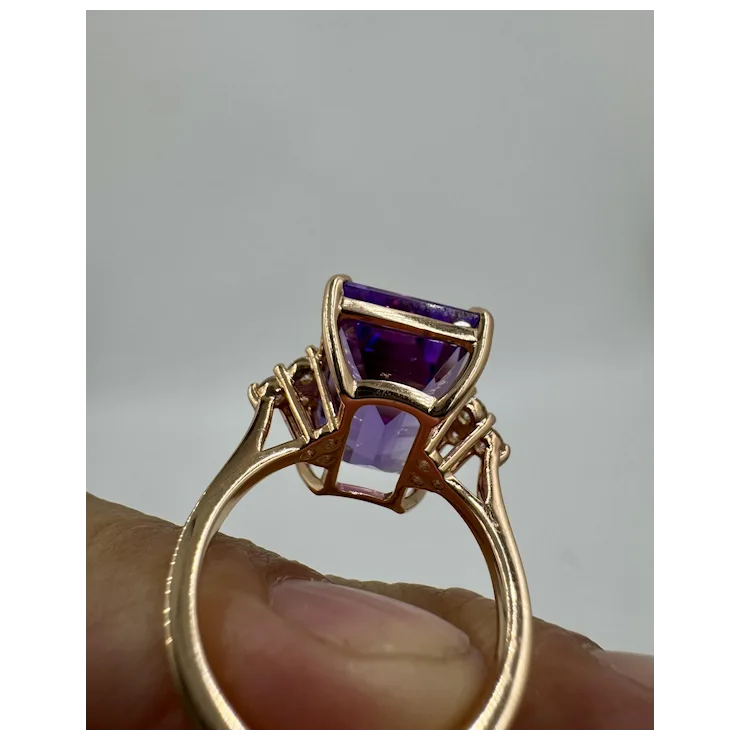 Gold ring with purple gemstones held by a hand against a gray background