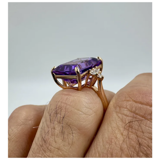 Gold ring with a purple gemstone on a finger against a gray background