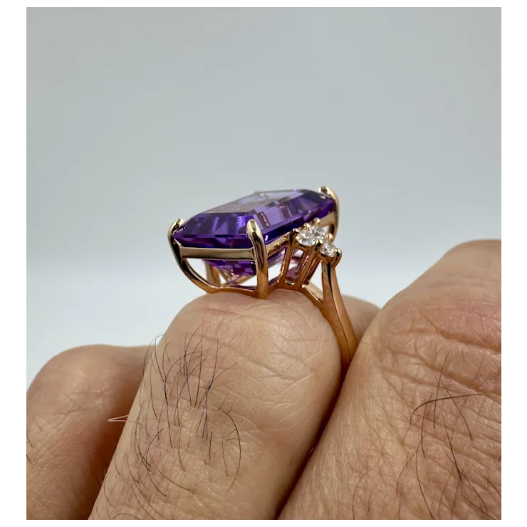 Gold ring with a purple gemstone on a finger against a gray background