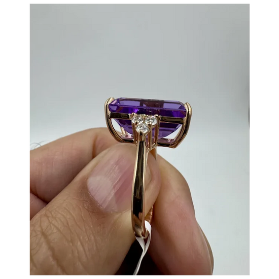 Gold ring with a purple gemstone held by a hand against a gray background