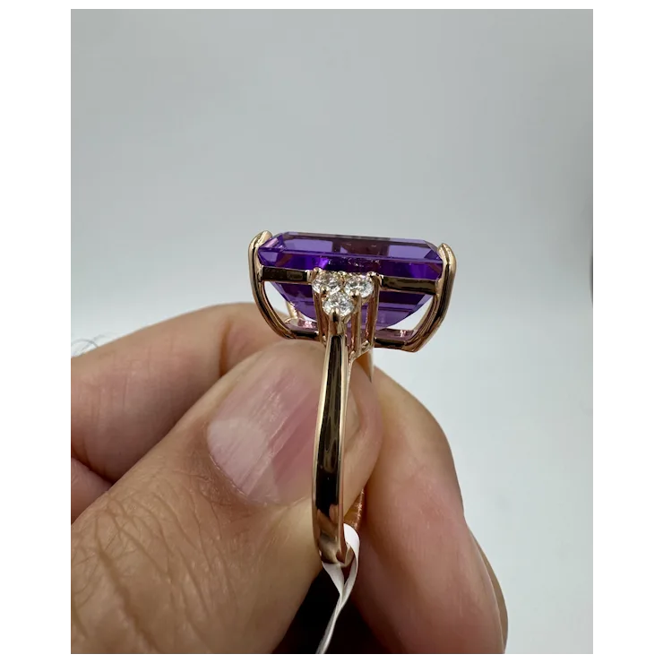 Gold ring with a purple gemstone held by a hand against a gray background