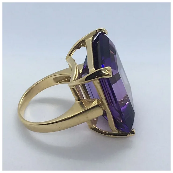Gold ring with a purple gemstone on a light gray background