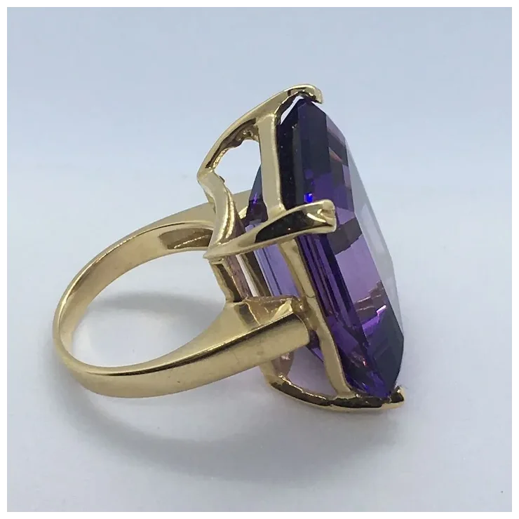 Gold ring with a purple gemstone on a light gray background