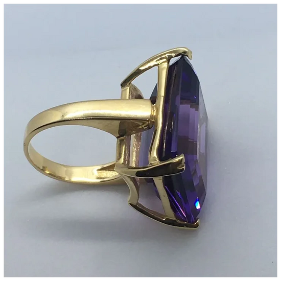 Gold ring with a large purple gemstone on a light gray background