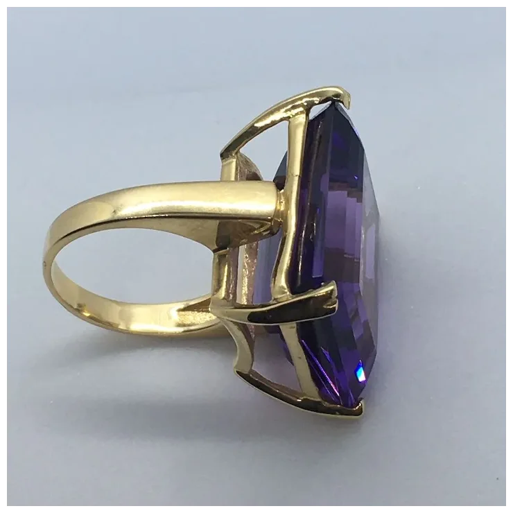 Gold ring with a large purple gemstone on a light gray background