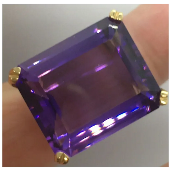Ring with a large purple gemstone and gold setting on a neutral background