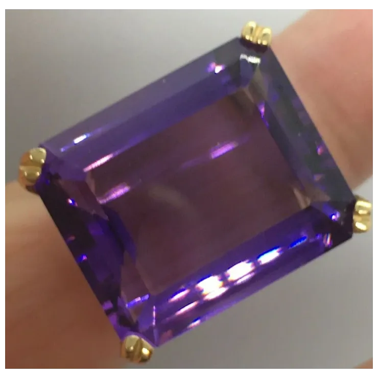 Ring with a large purple gemstone and gold setting on a neutral background