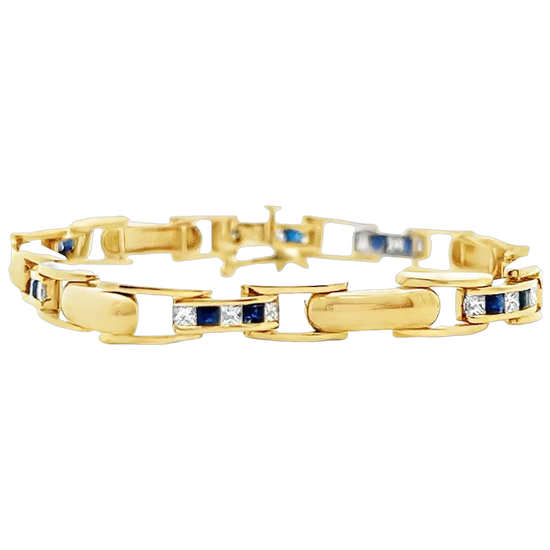 Gold bracelet with embedded blue and clear stones on a white background