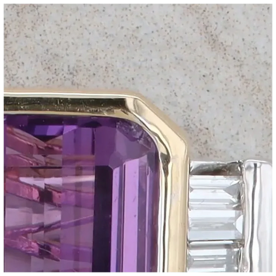 Close-up of a purple gemstone in a gold setting against a neutral background