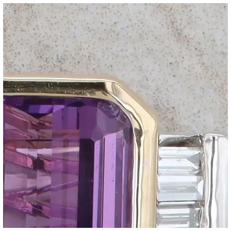 Close-up of a purple gemstone in a gold setting against a neutral background