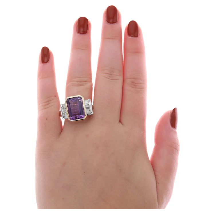 Ring with a purple gemstone on a hand with red nail polish against a white background