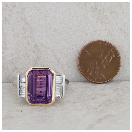 Ring with purple gemstone and diamond accents next to a penny on a marble surface