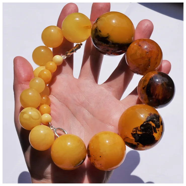 Hand holding a bracelet with yellow and brown beads against a white background