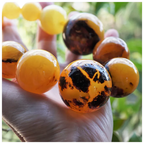 Close-up of amber beads with black inclusions held in a hand against a blurred natural background.