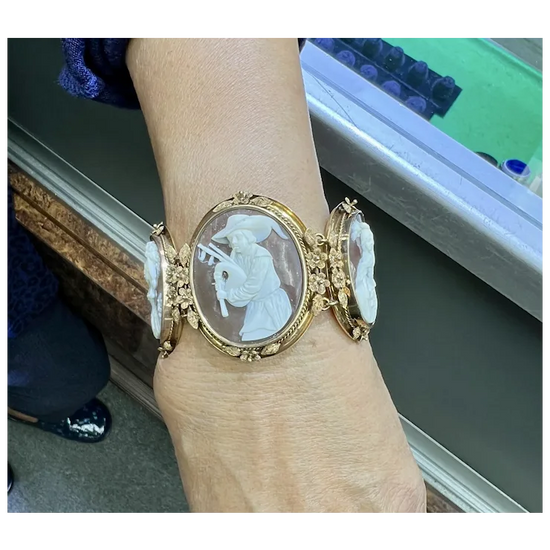 Gold bracelet with a cameo design worn on a wrist, with a blurred background.