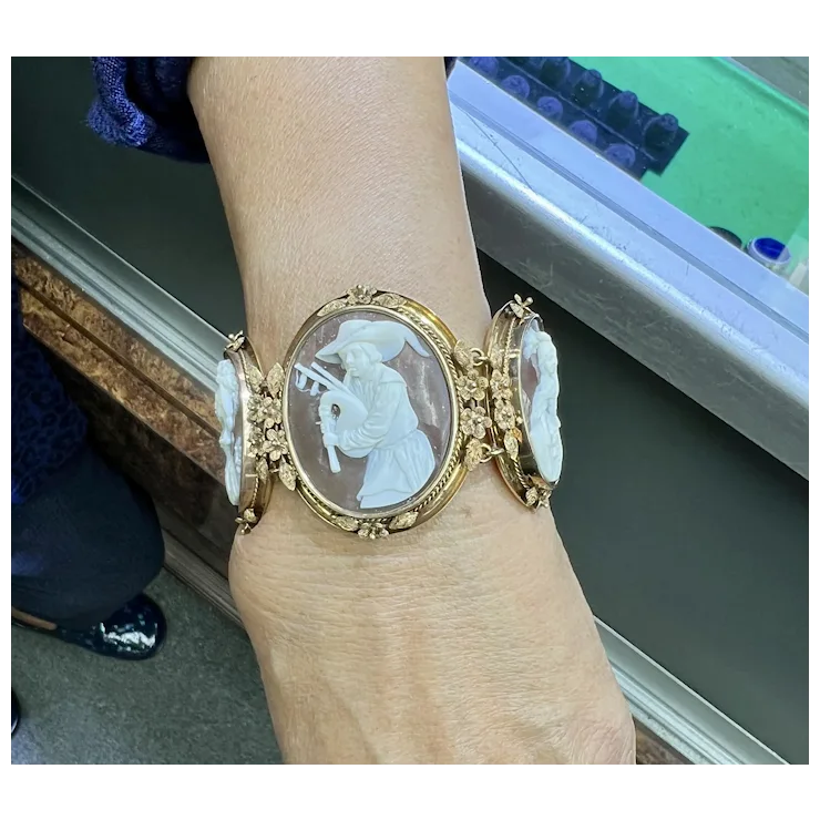 Gold bracelet with a cameo design worn on a wrist, with a blurred background.