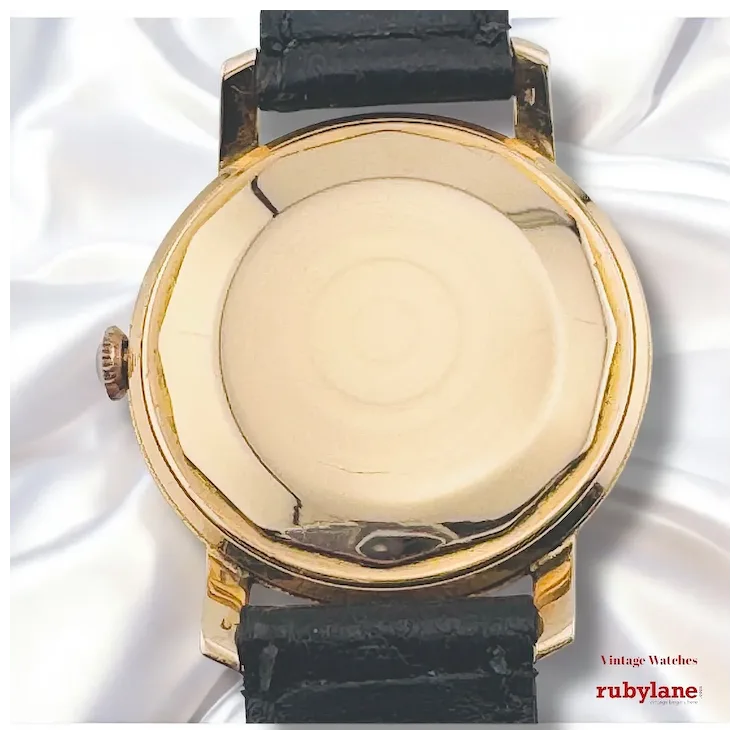 Vintage watch with gold case and black leather strap on a white background, branded 'rubylane'.