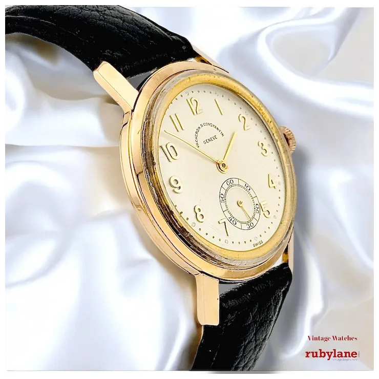 Gold wristwatch with black strap on a white fabric background, featuring Rubylane branding.
