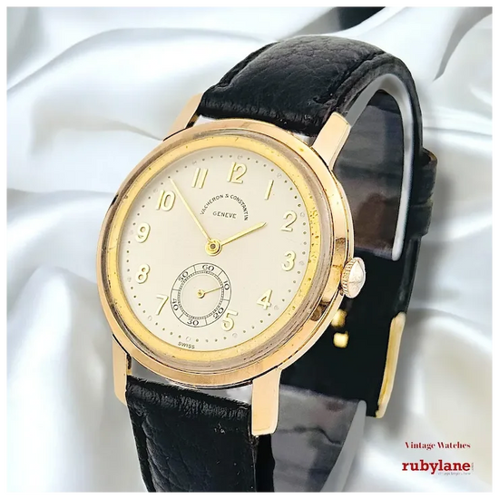 Vintage watch with black leather strap and gold case on a white background, featuring Rubylane branding.