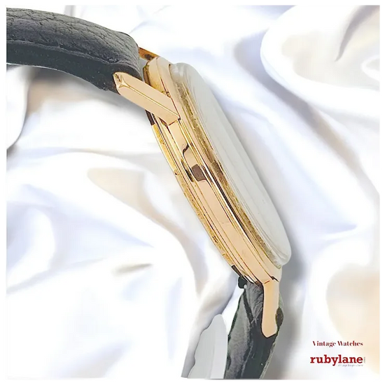 Gold and black watch on a white fabric background with Ruby Lane branding.