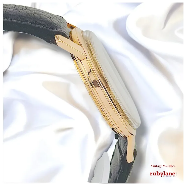 Gold and black watch on a white fabric background with Ruby Lane branding.
