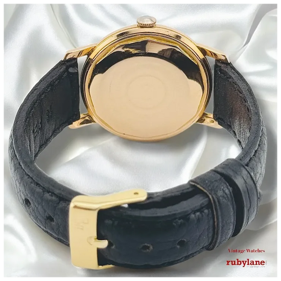 Vintage-style watch with gold case and black leather strap on a white background, featuring Rubylane branding.