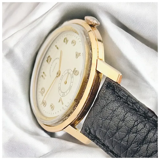 Gold watch with a black leather strap on a white fabric background
