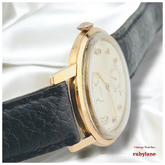 Vintage watch with gold case and black leather strap on a white background, featuring Ruby Lane branding.