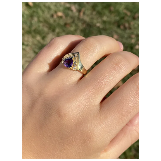 Gold ring with a purple gemstone on a hand against a blurred natural background