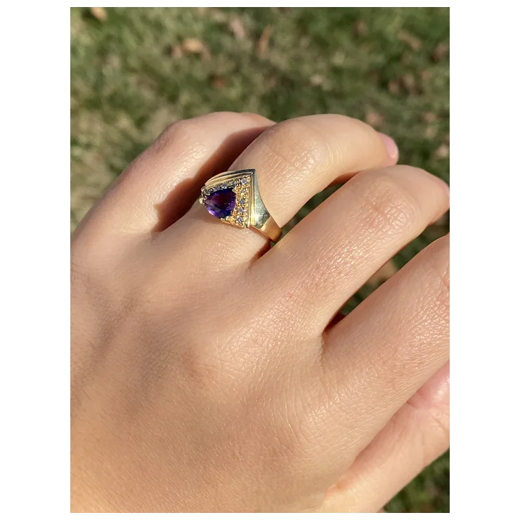 Gold ring with a purple gemstone on a hand against a blurred natural background