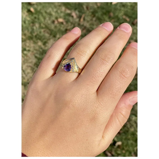 Gold ring with a purple gemstone on a hand against a blurred natural background