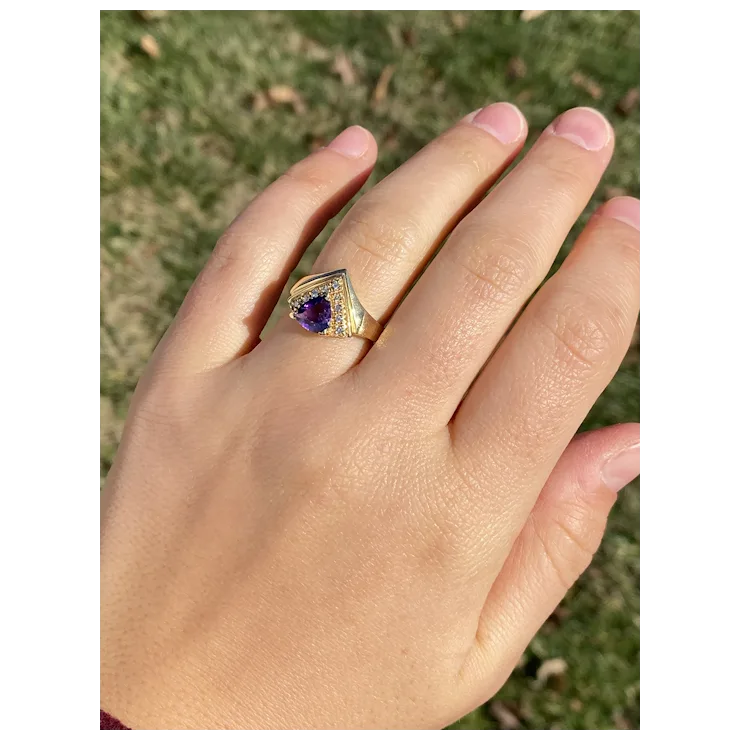 Gold ring with a purple gemstone on a hand against a blurred natural background