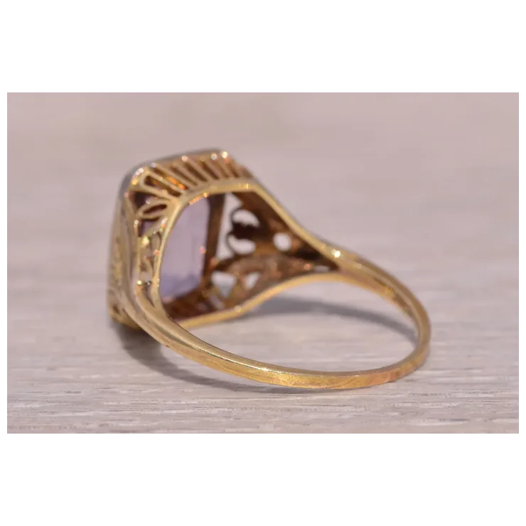 Gold ring with intricate design on a light wooden surface